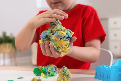 Little boy playing with bright kinetic sand at table in room, closeup
