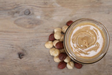 Tasty hazelnut nut paste in jar on wooden table, top view. Space for text