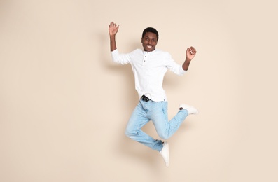 Full length portrait of African-American man jumping on color background