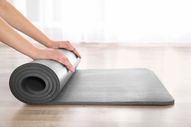 Photo of Woman rolling yoga mat on floor indoors, closeup