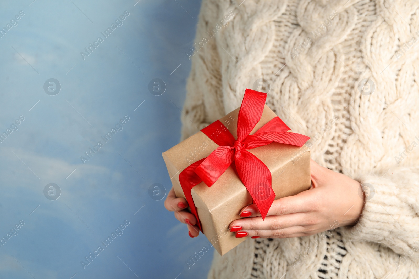 Photo of Young woman holding Christmas gift on blue background, closeup. Space for text