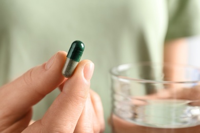 Photo of Woman holding spirulina pill and glass of water, closeup with space for text