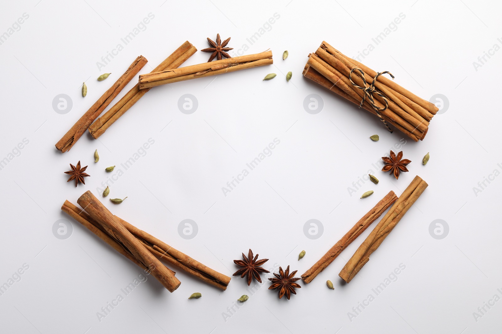 Photo of Frame made of cinnamon sticks, star anise and cardamom pods on white background, flat lay