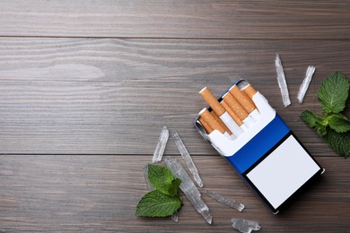 Photo of Pack of cigarettes, menthol crystals and mint on wooden table, flat lay. Space for text