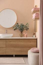Stylish mirror, eucalyptus branches, vessel sink and bathroom vanity. Interior design