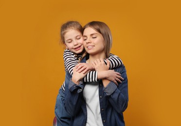 Photo of Little daughter hugging her mom on orange background. Happy Mother's Day