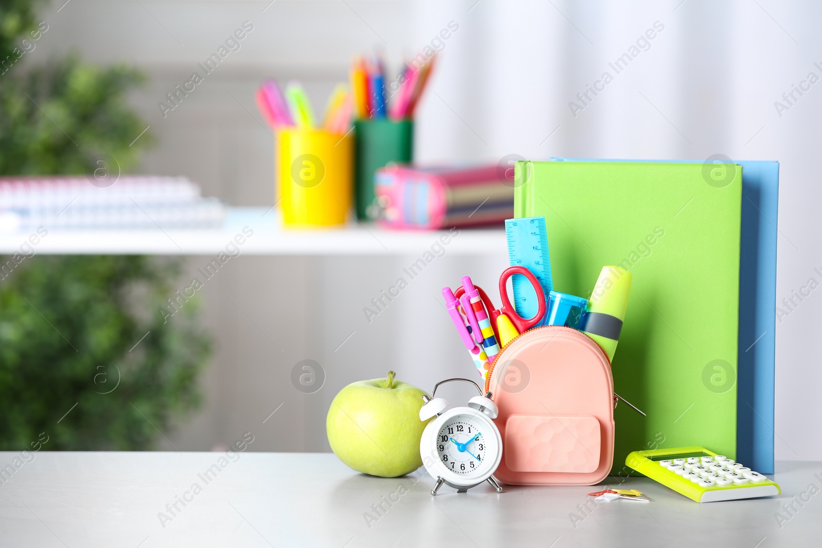 Photo of Alarm clock, apple and school stationery on white table. Space for text