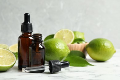 Photo of Lime essential oil and citrus fruits on marble table