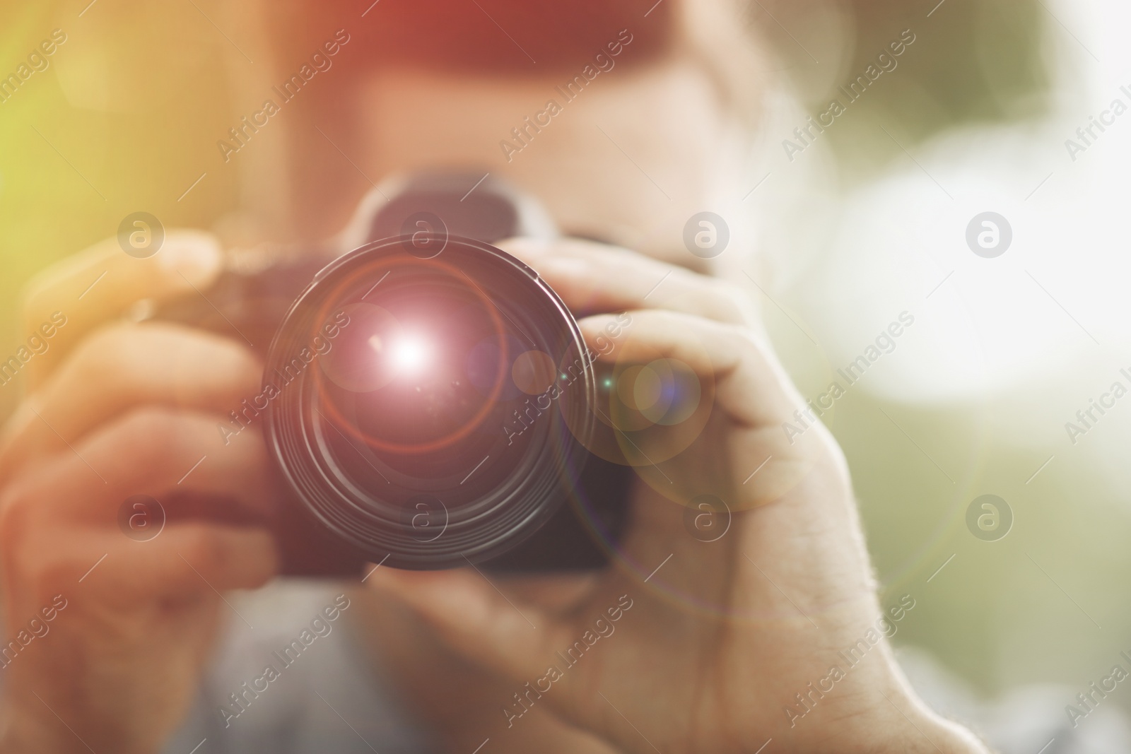 Image of Photographer taking picture with professional camera outdoors, focus on lens