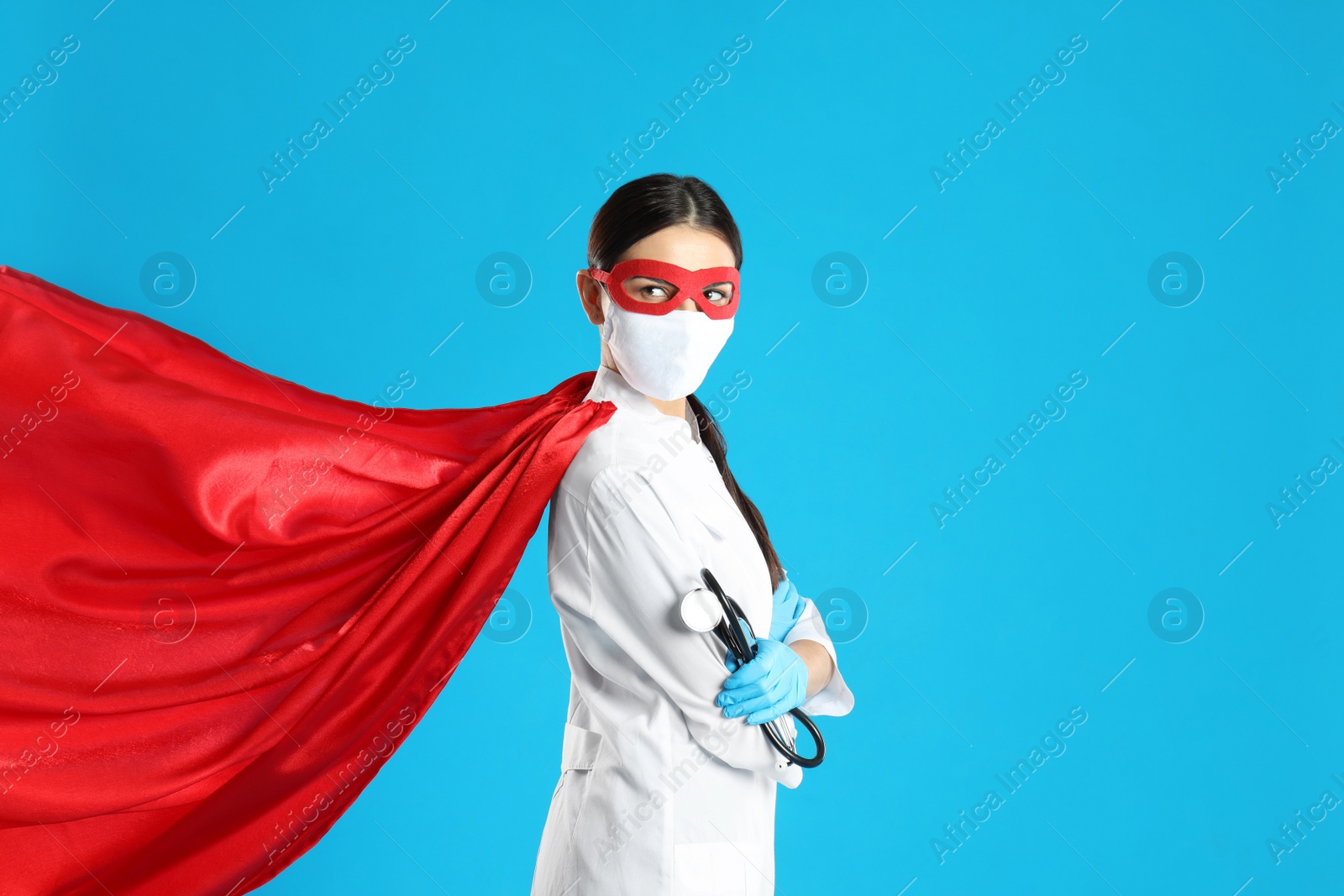 Photo of Doctor dressed as superhero posing on light blue background. Concept of medical workers fighting with COVID-19