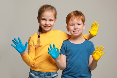 Photo of Little girl and boy with hands painted in Ukrainian flag colors on light grey background. Love Ukraine concept