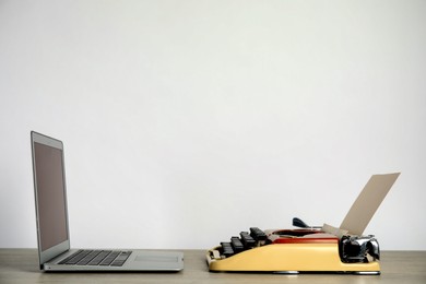 Old typewriter and laptop on table against light background, space for text. Concept of technology progress