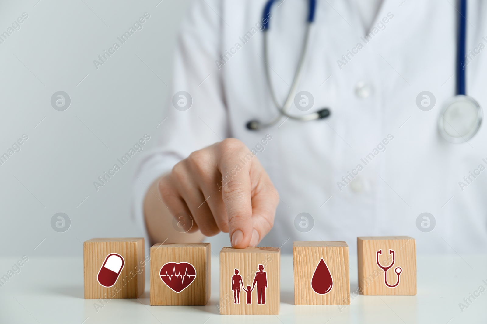 Image of Doctor and wooden cubes with different icons on white table, closeup. Insurance concept