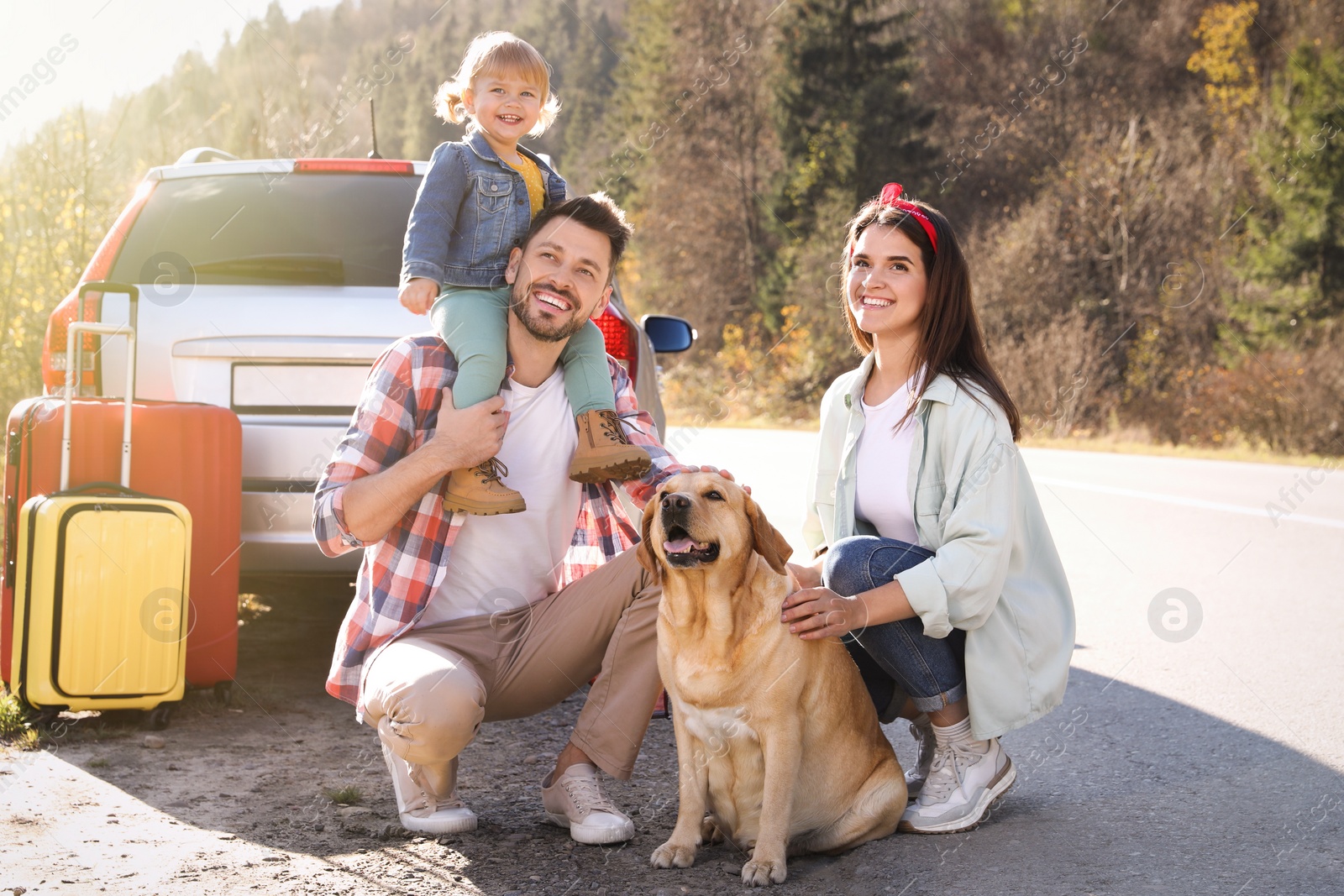 Photo of Parents, their daughter and dog near road. Family traveling with pet