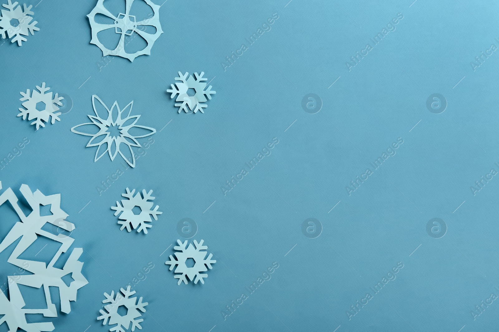 Photo of Many paper snowflakes on turquoise background, flat lay. Space for text