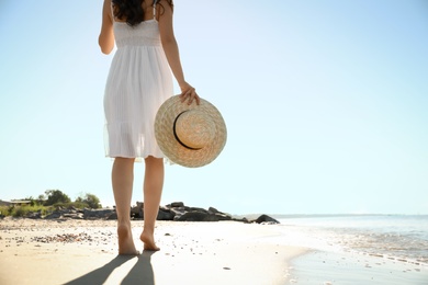 Young woman with hat walking on beach near sea, closeup. Space for text