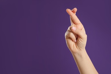 Photo of Woman holding fingers crossed on purple background, closeup with space for text. Good luck superstition
