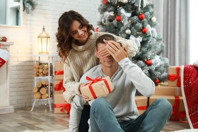 Young woman presenting Christmas gift to her boyfriend at home 