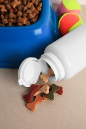 Bottle with vitamins, toys and dry pet food in bowl on beige background