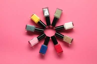 Photo of Bright nail polishes in bottles on pink background, flat lay