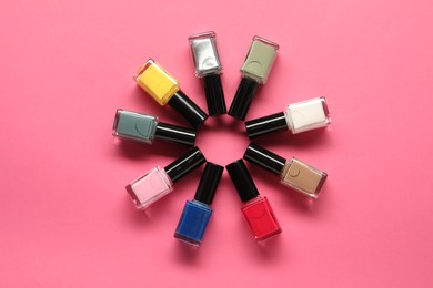 Bright nail polishes in bottles on pink background, flat lay