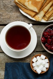 Photo of Cup of tea, cherry and crepes on wooden table, flat lay