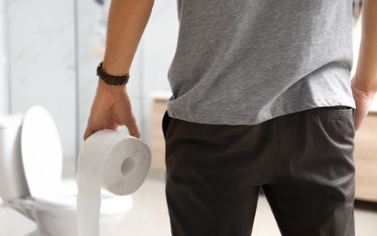 Photo of Man with paper roll near toilet bowl in bathroom, closeup