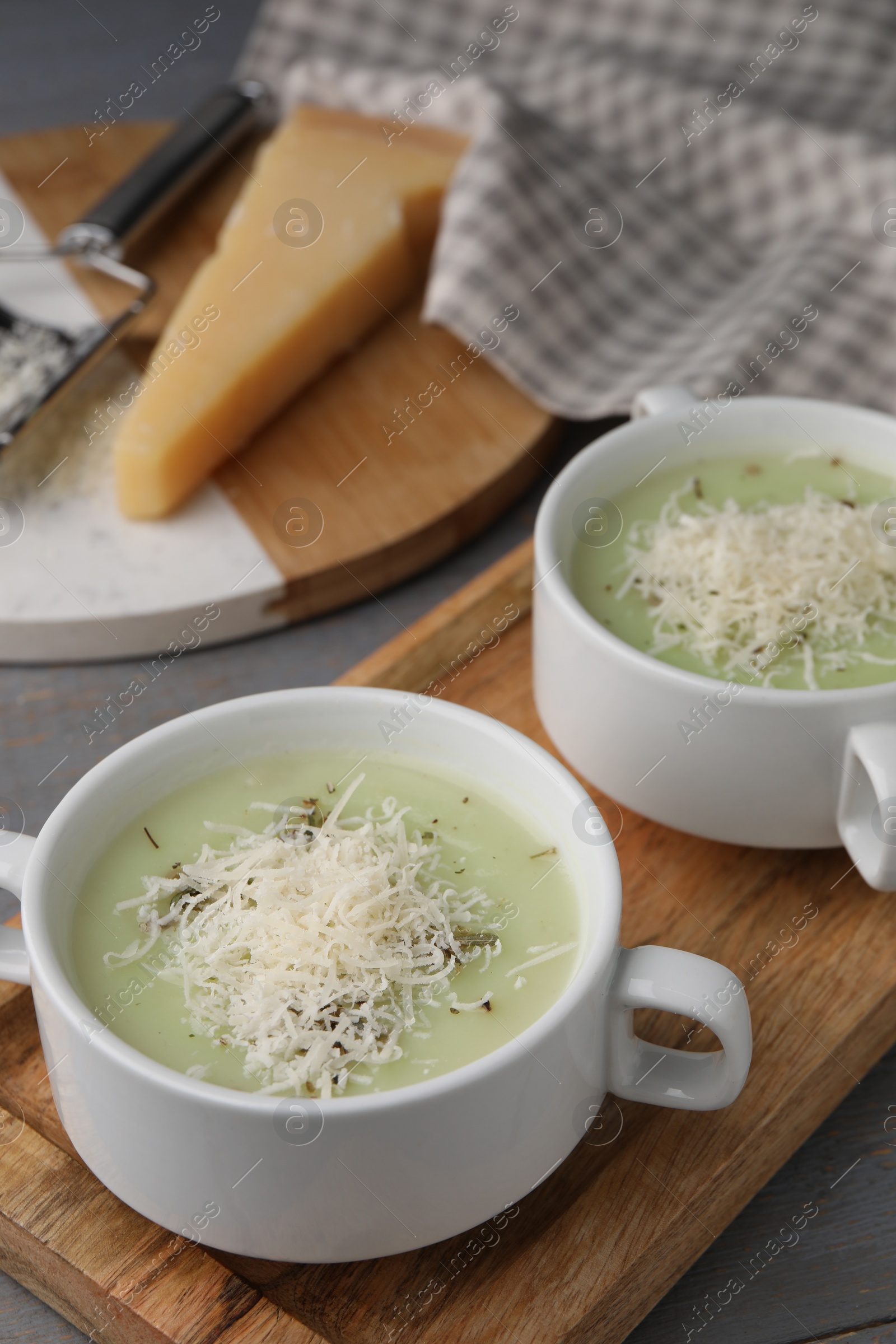 Photo of Delicious cream soup with parmesan cheese in bowls on grey wooden table