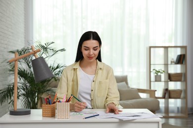 Photo of Young woman coloring antistress page at desk indoors