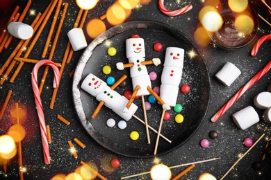 Image of Flat lay composition with funny snowmen made of marshmallows on black table. Bokeh effect