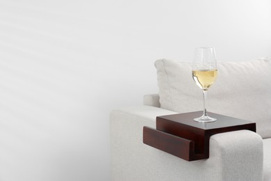 Glass of white wine on sofa with wooden armrest table indoors, space for text. Interior element