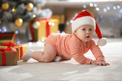 Photo of Little baby wearing Santa hat on floor indoors. First Christmas