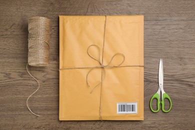 Photo of Padded envelope, rope and scissors on wooden background, flat lay