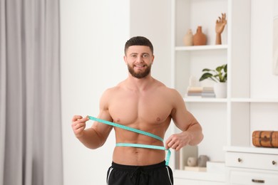Photo of Portraithappy athletic man measuring waist with tape at home. Weight loss concept