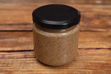 Photo of Tasty nut paste in jar on wooden table, closeup