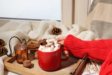 Photo of Woman with cup of cocoa at window, closeup. Winter drink