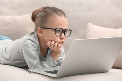 Photo of Little girl in glasses with laptop on sofa