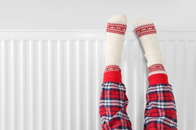 Photo of Little girl warming feet near heating radiator indoors, closeup. Space for text