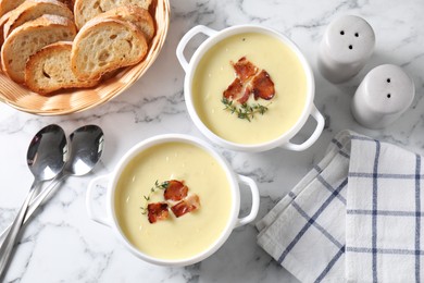 Photo of Tasty potato soup with bacon and rosemary in bowls served on white marble table, flat lay