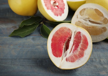 Photo of Fresh cut pomelo fruits with leaves on blue wooden table, closeup