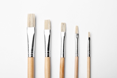 Different paint brushes on white background, top view