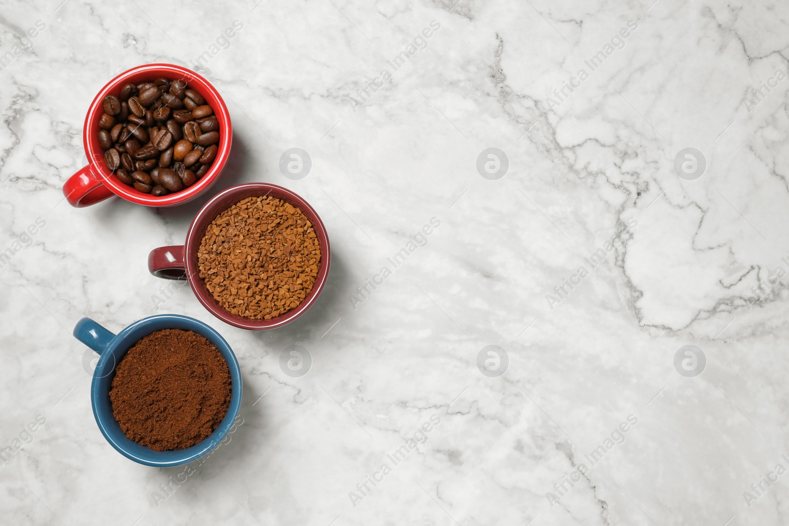 Photo of Instant, ground coffee and roasted beans in cups on white marble table, flat lay. Space for text