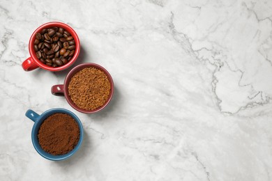 Photo of Instant, ground coffee and roasted beans in cups on white marble table, flat lay. Space for text