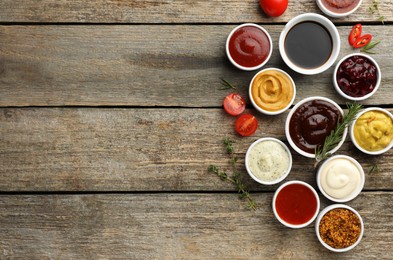 Photo of Different tasty sauces in bowls and ingredients on wooden table, flat lay. Space for text