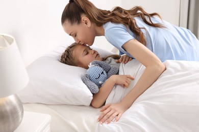 Photo of Happy mother kissing her cute daughter on bed at home