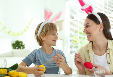 Photo of Happy mother and son with bunny ears headbands painting Easter eggs at home