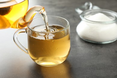 Photo of Pouring tasty tea into cup at grey table indoors, closeup