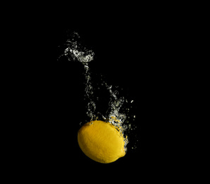 Photo of Ripe lemon falling down into clear water with splashes against black background