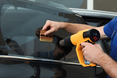 Photo of Worker tinting car window with heat gun in workshop, closeup