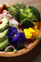 Photo of Delicious vegan bowl with broccoli, avocados and violet flowers on wooden table, closeup